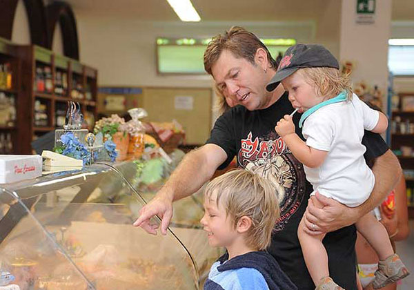 Una famiglia con due bambini sorridenti fa spesa al mini market del villaggio